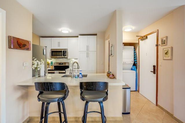 kitchen featuring white cabinets, stacked washer and clothes dryer, appliances with stainless steel finishes, light tile floors, and sink