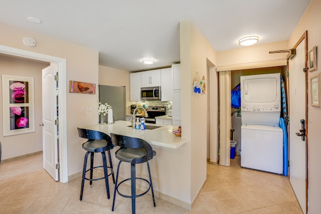 kitchen with stacked washer / dryer, stainless steel appliances, tasteful backsplash, white cabinets, and a breakfast bar