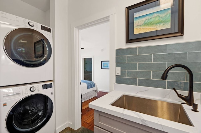 clothes washing area featuring dark hardwood / wood-style floors, sink, and stacked washer / dryer