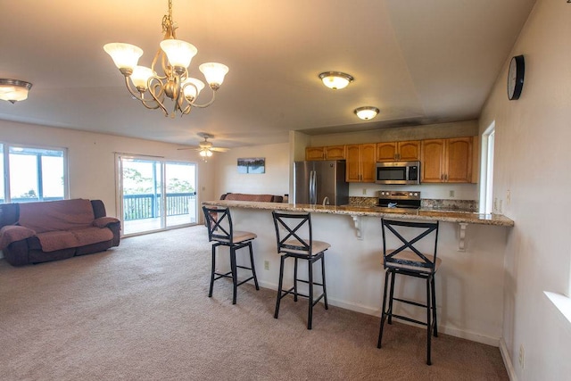 kitchen with light carpet, ceiling fan with notable chandelier, stainless steel appliances, and a kitchen breakfast bar