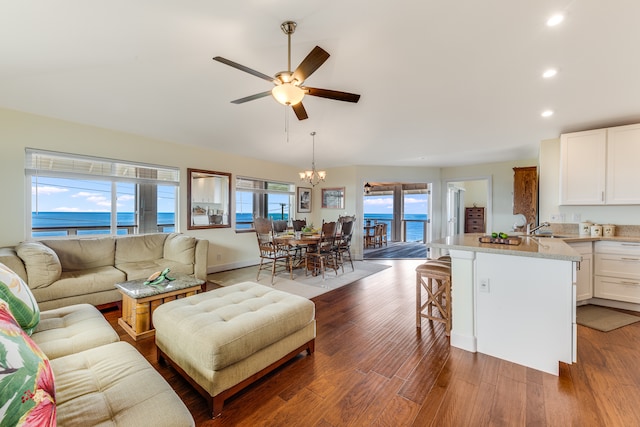 living room with hardwood / wood-style flooring, ceiling fan with notable chandelier, sink, and a water view