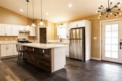 kitchen with a kitchen island, stainless steel refrigerator, white cabinetry, vaulted ceiling, and pendant lighting