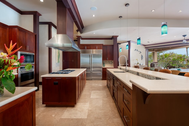 kitchen featuring wall chimney range hood, hanging light fixtures, a kitchen island with sink, built in appliances, and sink