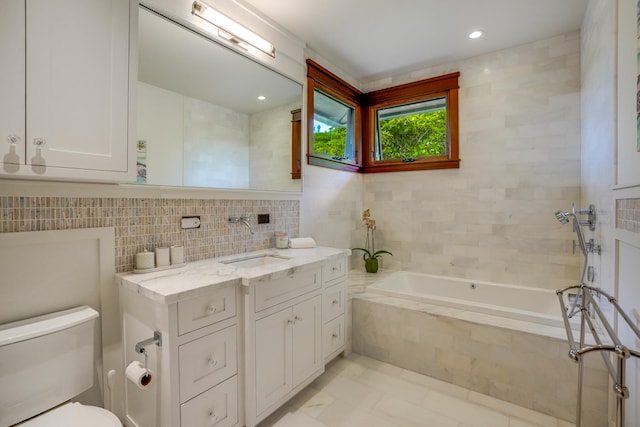 bathroom with tile walls, a relaxing tiled tub, vanity, tile patterned floors, and toilet