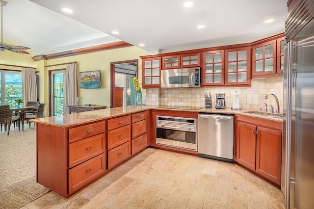 kitchen featuring kitchen peninsula, stainless steel appliances, sink, light stone counters, and tasteful backsplash