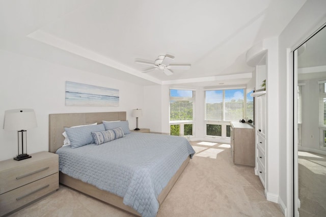 bedroom with light colored carpet, ceiling fan, and a tray ceiling