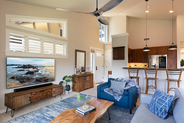 carpeted living room with ceiling fan and a towering ceiling