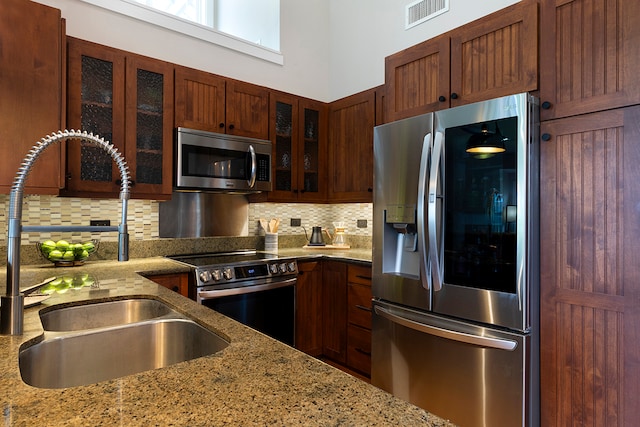 kitchen with tasteful backsplash, appliances with stainless steel finishes, sink, and light stone counters