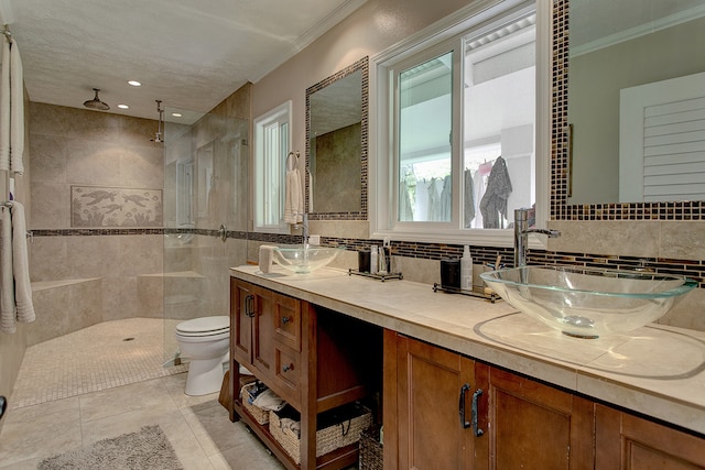 bathroom featuring tiled shower, toilet, tile floors, ornamental molding, and dual bowl vanity