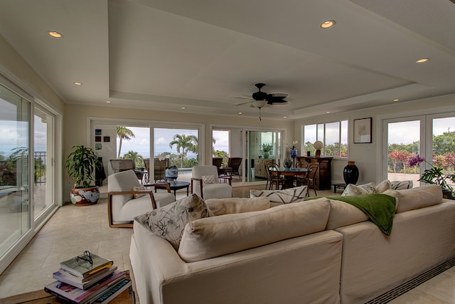 living room with a raised ceiling, ceiling fan, and light tile floors