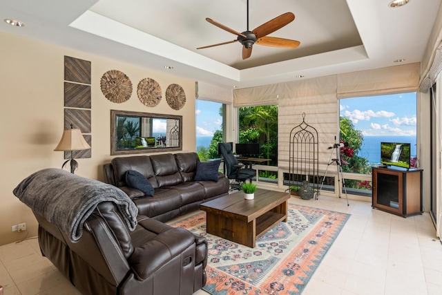 living room featuring a water view, ceiling fan, light tile flooring, and a raised ceiling