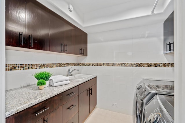 clothes washing area with tile walls, sink, washing machine and dryer, and light tile floors