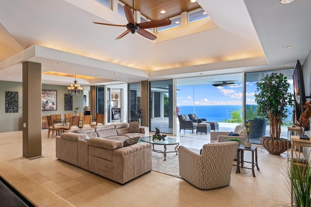 living room with light tile flooring, ceiling fan with notable chandelier, a tray ceiling, a water view, and a wall of windows