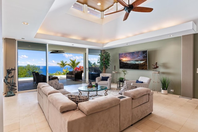 living room featuring a water view, ceiling fan, a tray ceiling, and light tile floors