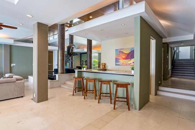 kitchen with kitchen peninsula, ceiling fan, light tile flooring, and a breakfast bar area