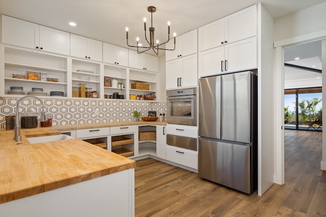 kitchen with stainless steel appliances, butcher block counters, pendant lighting, white cabinets, and hardwood / wood-style flooring