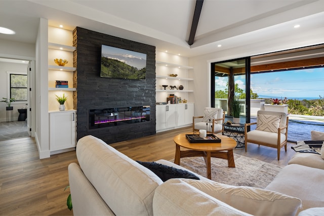 living room featuring a large fireplace, a wealth of natural light, hardwood / wood-style floors, beam ceiling, and built in shelves