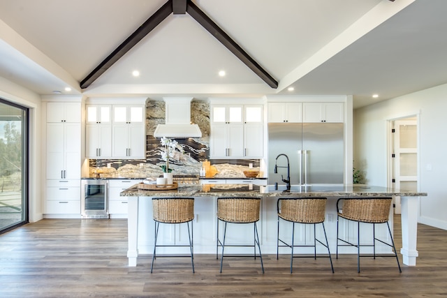 kitchen with wine cooler, white cabinetry, an island with sink, and built in refrigerator