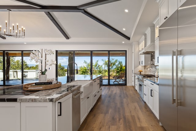 kitchen with white cabinetry, vaulted ceiling with beams, stainless steel appliances, a kitchen island with sink, and pendant lighting