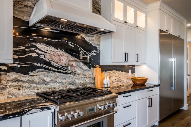 kitchen with custom range hood, dark hardwood / wood-style floors, white cabinetry, premium appliances, and dark stone countertops