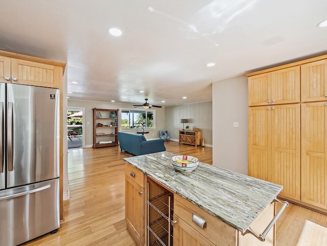 kitchen with light stone countertops, stainless steel fridge, light hardwood / wood-style flooring, ceiling fan, and light brown cabinetry