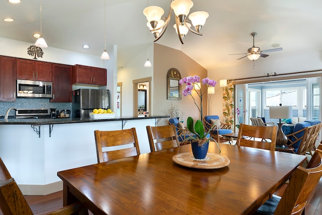 dining room with dark hardwood / wood-style floors, ceiling fan with notable chandelier, and vaulted ceiling