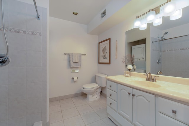 bathroom featuring stacked washer and clothes dryer, vanity, a tile shower, tile patterned floors, and toilet