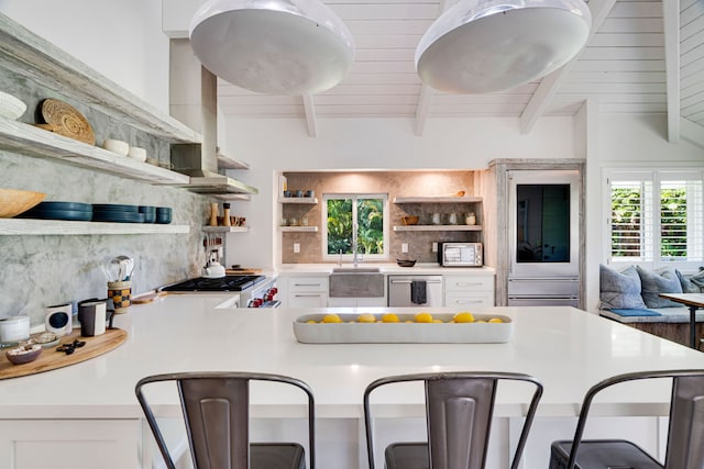 kitchen featuring beamed ceiling, white cabinetry, backsplash, wall chimney range hood, and stainless steel appliances