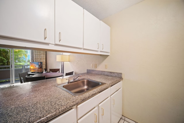 kitchen with a textured ceiling, white cabinetry, and a sink