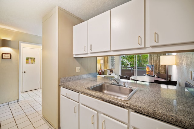 kitchen featuring light tile patterned floors, white cabinets, a textured ceiling, and a sink