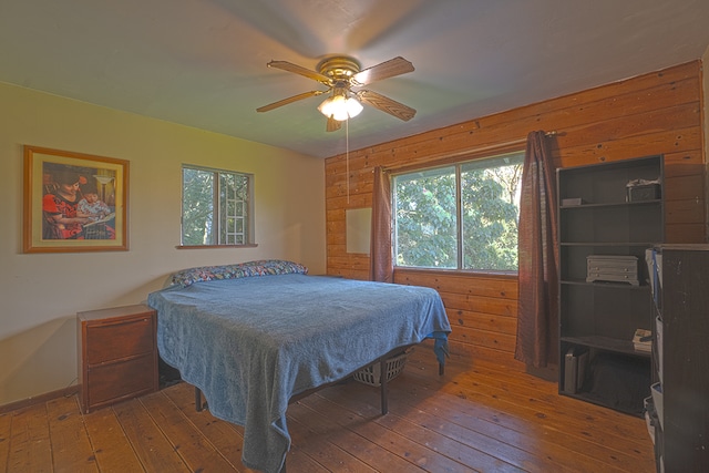 bedroom featuring ceiling fan, hardwood / wood-style flooring, and wooden walls