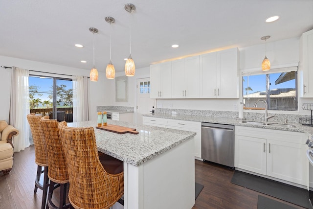 kitchen featuring a healthy amount of sunlight, a kitchen island, stainless steel dishwasher, white cabinets, and a sink