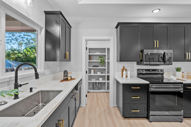 kitchen with light stone countertops, sink, appliances with stainless steel finishes, and light hardwood / wood-style flooring