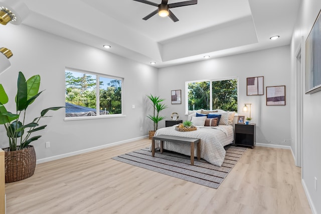 bedroom featuring ceiling fan, a raised ceiling, light hardwood / wood-style flooring, and multiple windows