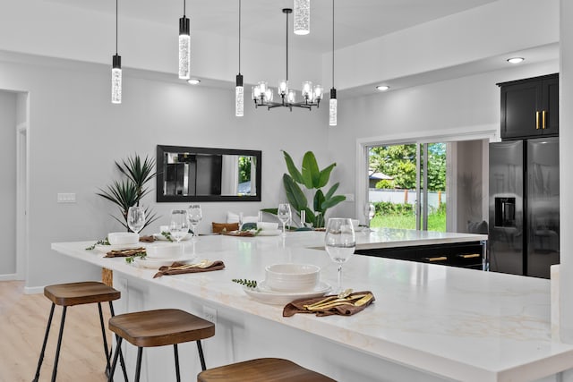 kitchen featuring decorative light fixtures, light stone countertops, stainless steel fridge with ice dispenser, and light hardwood / wood-style flooring