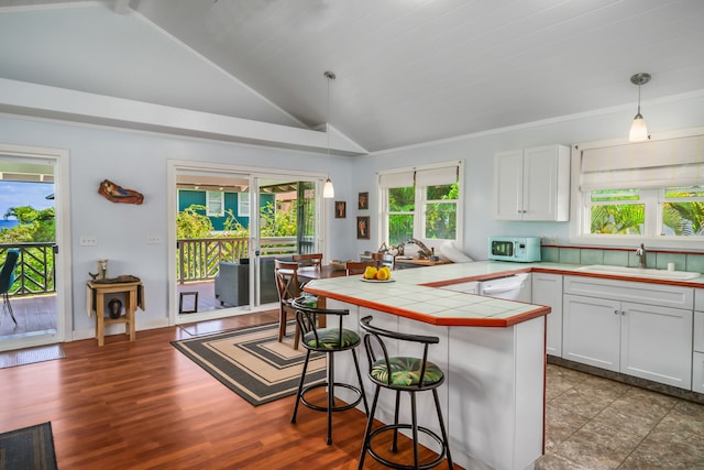 kitchen with hanging light fixtures, white cabinets, tile countertops, sink, and a breakfast bar