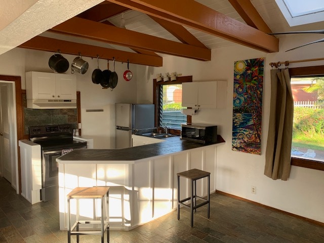 kitchen featuring white cabinets, vaulted ceiling with skylight, kitchen peninsula, stainless steel appliances, and tasteful backsplash