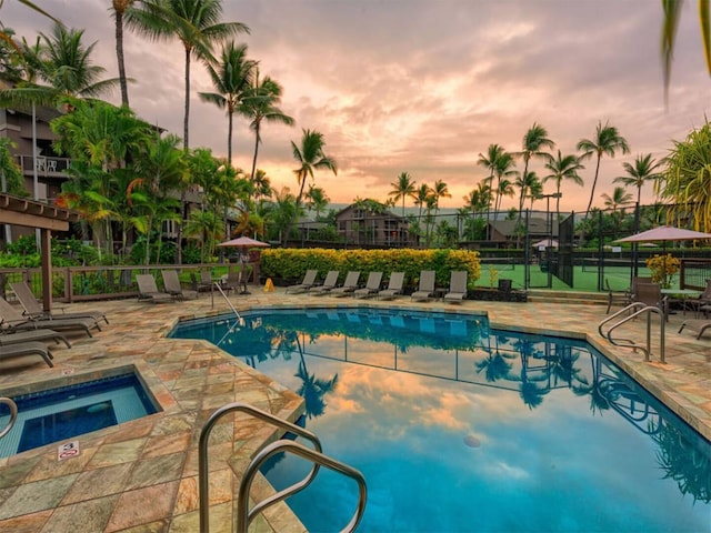 pool at dusk featuring a hot tub, a community pool, fence, and a patio