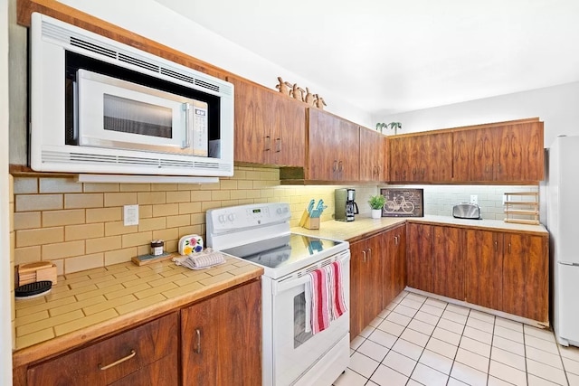 kitchen with light tile patterned floors, white appliances, light countertops, backsplash, and brown cabinets