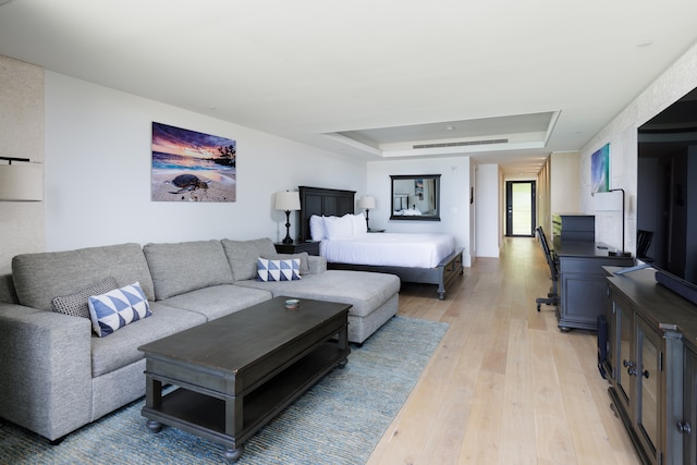 living room with a raised ceiling and light wood-type flooring