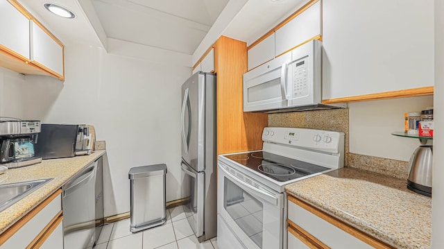 kitchen with stainless steel appliances, white cabinetry, light tile flooring, and light stone countertops