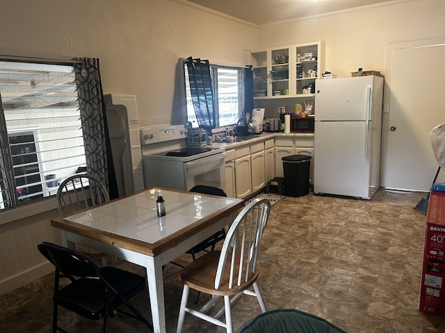 kitchen featuring crown molding, tile counters, glass insert cabinets, a sink, and white appliances