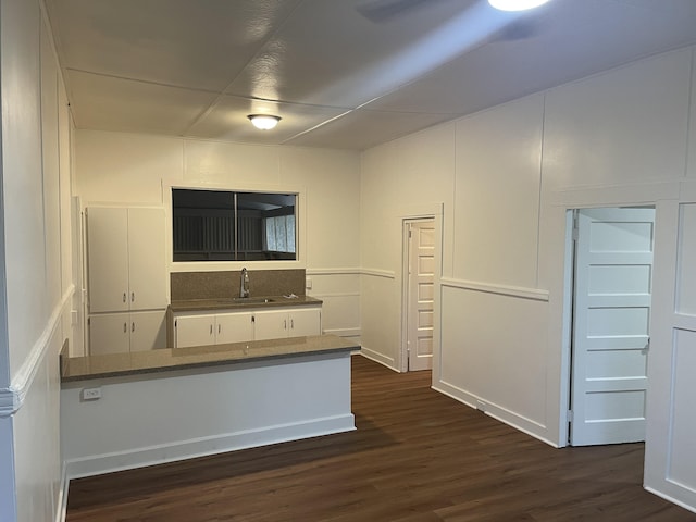 kitchen with a decorative wall, a peninsula, a sink, white cabinets, and dark wood-style floors