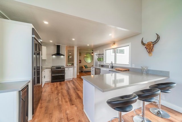 kitchen featuring appliances with stainless steel finishes, kitchen peninsula, wall chimney exhaust hood, backsplash, and a breakfast bar