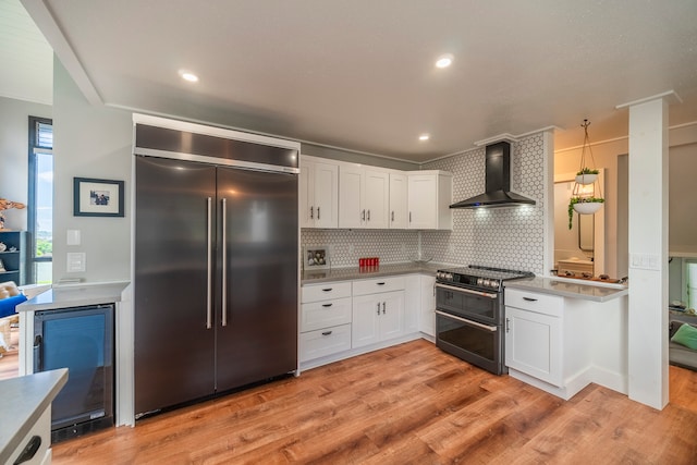 kitchen featuring light hardwood / wood-style floors, backsplash, high end appliances, wall chimney exhaust hood, and white cabinets