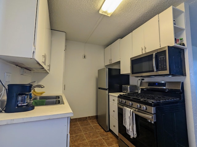 kitchen featuring appliances with stainless steel finishes, a textured ceiling, sink, dark tile patterned flooring, and white cabinetry