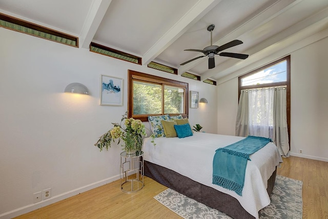 bedroom featuring multiple windows, ceiling fan, hardwood / wood-style floors, and vaulted ceiling with beams