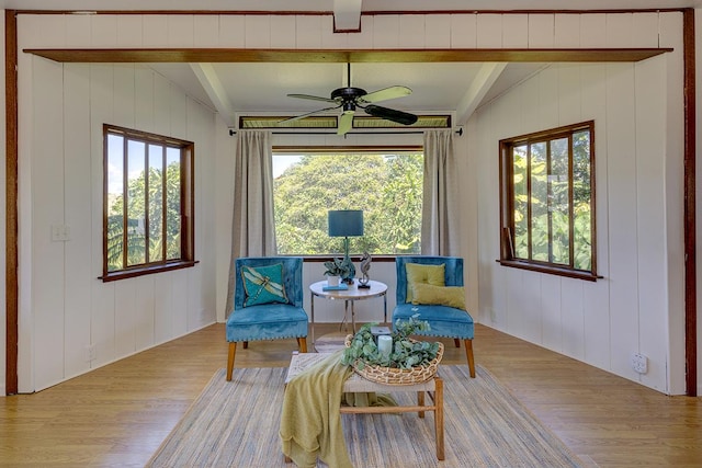 sitting room featuring ceiling fan, light hardwood / wood-style flooring, lofted ceiling with beams, and wood walls