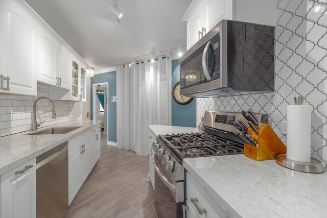 kitchen with track lighting, white cabinets, sink, decorative backsplash, and stainless steel appliances