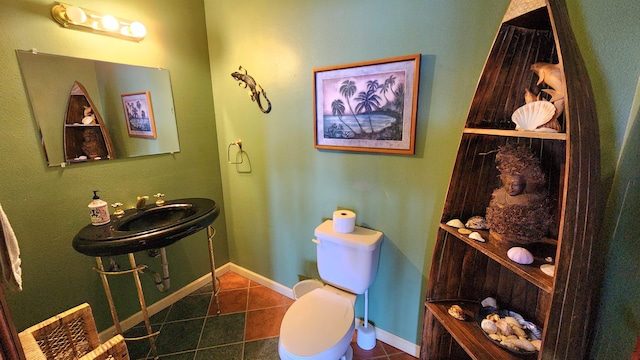 half bathroom featuring toilet, baseboards, a sink, and tile patterned floors